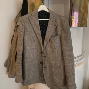 Beige kavaj från Gutteridge - Snygg beige kavaj från Gutteridge i linne. Stilren design med två knappar framtill och klassisk passform. Storlek 48 i herr.