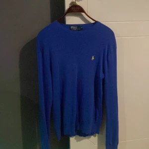 Blå tröja från Polo Ralph Lauren - Säljer en snygg blå tröja från Polo Ralph Lauren i storlek M. Tröjan har en klassisk design med långärmade ärmar och det ikoniska gula logotypbroderiet på bröstet. Perfekt för både vardag och fest! 💙