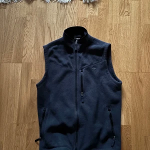 Svart fleeceväst från Timberland - Säljer en svart fleeceväst från Timberland i slim fit. Västen har en dragkedja framtill och två praktiska fickor med dragkedjor. Perfekt för lager-på-lager under kyliga dagar. Den är i mycket bra skick och redo för nya äventyr!