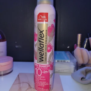 Torrschampo  - En flaska Wellaflex torrschampo i doften Sensual Rose. Den lovar 10-i-1 fördelar för håret, inklusive fräschhet och volym. Flaskan har en rosa och vit design med blommönster.