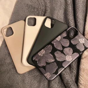 4x Fodral för mobiltelefon i olika färger, iPhone 11 - Säljer ett set med fyra mobilfodral i olika färger och mönster. Ett fodral är svart med blommigt mönster, medan de andra är enfärgade i beige, vit och svart. Perfekt för att byta stil på din mobil!