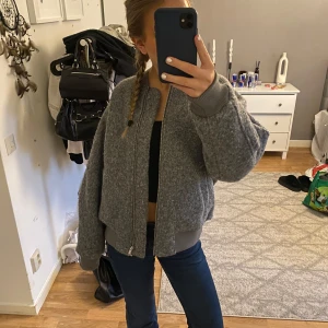 Grå bomberjacka - Säljer en snygg grå bomberjacka med dragkedja framtill och ribbade muddar. Jackan har en cool ficka med dragkedja på ärmen och en bekväm, oversized passform. Perfekt för en avslappnad stil. Aldrig använd 🥰