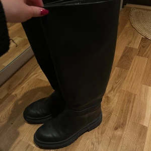 Svarta stövlar från NA-KD - Snygga svarta stövlar från NA-KD med dragkedja på insidan. De är i storlek 36 och är använda ett fåtal gånger.Tillverkade i syntetmaterial med en klassisk design. 