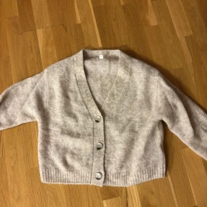 Beige kofta med knappar - Mysig beige kofta med knappar framtill. Den har en v-ringad design och ribbade kanter. Perfekt för kyligare dagar. Pris kan diskuteras.