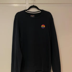 Mörkblå tröj från Abercrombie & Fitch - Säljer en stilren mörkblå tröja från Abercrombie & Fitch med ett färgglatt peace-märke på bröstet. Tröjan har långa ärmar och en klassisk rund halsringning. Perfekt för en avslappnad look.