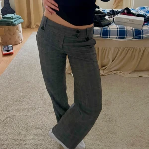 Grå rutig lågmidjad kostymbyxa  - Snygga mörkgråa byxor med rutig design från InWear. De har en låg midja och stängs med två knappar framtill. Byxorna har en rak/ utsvängd passform och är perfekta för både avslappnad och stilren stil.