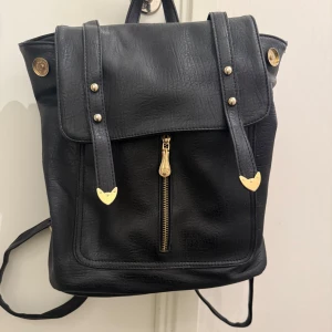 Svart Ryggsäck  - En väldigt fin svart ryggsäck med gulddetaljer. Jag kommer tyvärr inte ihåg vart den är köpt. Den är i mycket bra skick och har inte använts mycket. Den rymmer mycket och passar perfekt till olika saker ex. Skola, jobb, resor, osv🤍