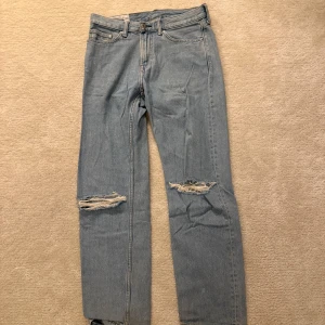 Blå jeans med slitningar - Snygga blå jeans med slitningar på knäna. Relaxed fit. Storlek 31/32. Byxan är i mycket bra skick och är knappt använd.. 