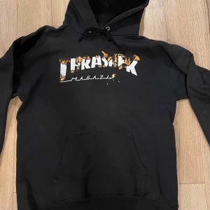 Thrasher hoodie svart - Säljer en svart hoodie från Thrasher med ett coolt tryck på framsidan. Hoodien har en klassisk design med känguruficka och justerbar huva. Perfekt för en avslappnad stil. Ärmarna är slitna som man ser på bilden. Sitter som medium