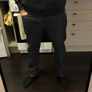 Nudie Jeans - Snygga mörkblå jeans med normal passform och klassisk design. Byxorna har en rak stil och är perfekta för en avslappnad look. De har fickor både fram och bak samt en dragkedja. Storleken är 34/30 och jag på bilden är 185 och väger ca 84 kg! Använda endast en gång‼️‼️