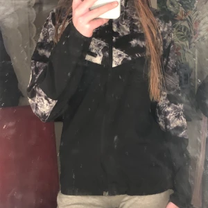 Svart och mönstrad jacka med dragkedja - Snygg svart jacka med unikt mönster i grått och vitt. Jackan har en dragkedja framtill och en praktisk bröstficka med dragkedja. Perfekt för en cool och avslappnad stil.