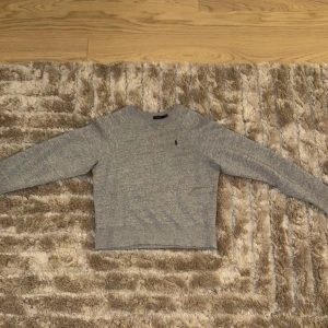 Grå tröja från Ralph Lauren - Säljer en stilren grå tröja från Ralph Lauren med det klassiska logotypbroderiet på bröstet. Tröjan har långa ärmar och en rund halsringning, perfekt för en avslappnad look. Tröjan är i väldigt gott skick och har använts sparsamt!