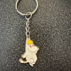 Nyckelring med Muminmotiv Snorkfröken  - Charmig nyckelring med en figur från Mumindalen. Den har en söt design med en vit kropp och gul detalj på huvudet. Perfekt för att ge dina nycklar en personlig touch.