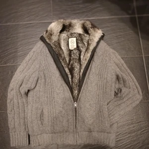 Pälsfodrad Cardigan Gant - Säljer en väldigt mysig och tjock pälsfodrad cardiganjacka från Gant, perfekt nu till kallare väder. Den är i fint skick och har en stilren design. Extremt tjock och fin päls samt fodring i armarn vilket gör den väldigt bekväm. Skriv vid minsta fundering!