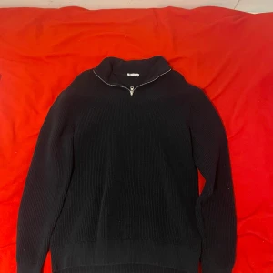 Svart kvartszip - Säljer en svart kvartszip tröja med dragkedja i kragen. Perfekt för kyligare dagar med sin stilrena design och bekväma passform. Tröjan har långa ärmar och en hög krage som kan justeras med dragkedjan. Om du vill ha fler bilder är det bara att skriva! Nypriset på den här är 650kr så det är ett bra pris.