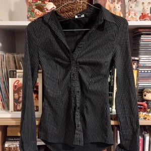 Svart och vit randig skjorta - Snygg svart skjorta med vita ränder och långa ärmar. Skjortan har en klassisk krage och knappar framtill. Perfekt för en stilren look.