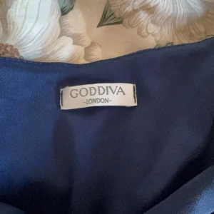 Mörkblå långklänning från Goddiva London - Elegant mörkblå långklänning från Goddiva London med korta ärmar och ett knytband i midjan. Perfekt för en stilfull look.