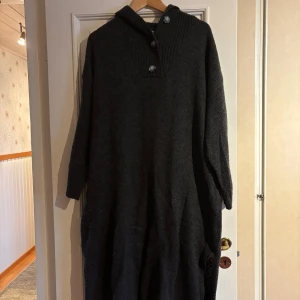 Mörkgrå stickad tröja med knappar - Säljer en mysig mörkgrå stickad tröja med ribbad struktur och knappar vid halsen. Perfekt för kyliga dagar med sin långa passform och bekväma design. Storlek XL/2XL.