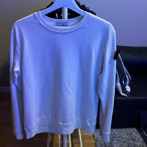 Vit sweatshirt från Stone Island - Säljer en stilren vit sweatshirt från Stone Island. Tröjan har en klassisk rund halsringning och långa ärmar. Perfekt för en avslappnad och trendig look. Skriv dm vid funderingar! Inga defekter