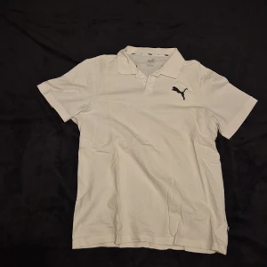 Vit kortärmad pikétröja från Puma - Säljer en stilren vit pikétröja från Puma med korta ärmar och klassisk krage. Tröjan har en broderad Puma-logga på bröstet. Perfekt för en avslappnad och sportig look.