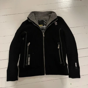 Fodrad Cardigan jacka - Säljer en riktigt fet svart stickad cardigan jacka med grått foder inuti. Jackan har dragkedja framtill och flera praktiska fickor med dragkedjor. Perfekt för kyligare dagar