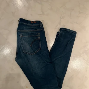 Mörkblå jeans från Dondup - Snygga mörkblå jeans från Dondup med klassisk femficksdesign och knappgylf. Jeansen har en diskret tvättad look och orange sömmar som ger en cool kontrast. Perfekta för en avslappnad stil.
