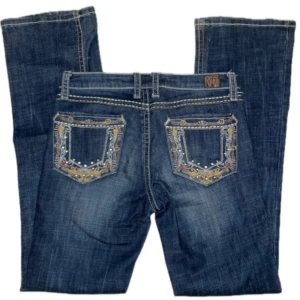 Blå wrangler jeans med broderade detaljer - Sååå snygga lågmidjadw blåa jeans från Wrangler Rock 47 med unika broderade detaljer på bakfickorna. 