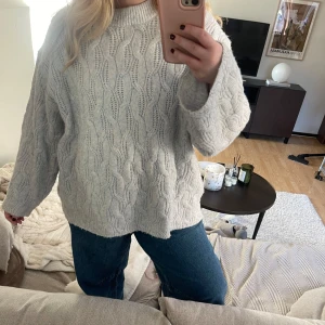 ljusblå stickad tröja - Mysig ljusblå stickad tröja med kabelstickat mönster. Tröjan har en avslappnad passform och långa ärmar, perfekt för kyliga dagar. Enkel att matcha med jeans eller kjol för en stilren look.
