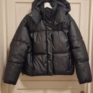 Svart pufferjacka från FB Sister - Snygg svart pufferjacka från FB Sister i storlek M. Jackan har en hög krage och dragkedja framtill. Perfekt för kyliga dagar med sin vadderade design.
