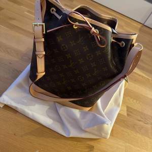 Snygg axelväska med klassiskt mönster och justerbar rem. Väskan har en praktisk dragsko och detaljer i ljusbrunt läder. Perfekt för att bära dina dagliga nödvändigheter med stil. Dustbag ingår!