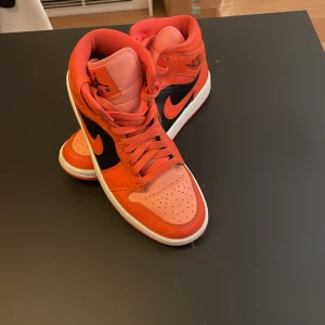 Nike Air Jordans i orange och svart - Snygga Nike Air Jordans i en djärv orange och svart färgkombination. Skorna har klassisk snörning och en hög siluett som ger ett sportigt utseende. Perfekta för dig som vill sticka ut med stil.