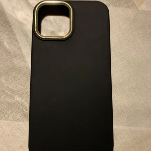 Svart mobilskal med gulddetaljer, använd bara 1 gång tyvärr passade den inte min mobil. Om ni tycker det kosta för mycket kan vi diskutera om priset! - Snyggt svart mobilskal med stilrena gulddetaljer runt kamerauttaget. Skalet har en slimmad design och är perfekt för att skydda din telefon samtidigt som det ger en elegant look. Passar perfekt för dig som vill ha både stil och funktion. 