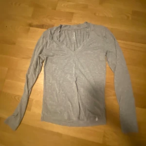 Grå långärmad tröja - Säljer en stilren grå långärmad tröja med v-ringning. Perfekt för lager-på-lager under kyligare dagar. Enkel och bekväm design som passar till det mesta.