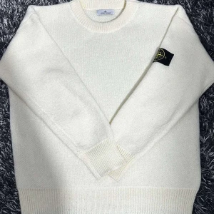 Vit stickad tröja från Stone Island - Säljer en stilren vit stickad tröja från Stone Island. Tröjan har en klassisk rund halsringning och långa ärmar. Den ikoniska Stone Island-loggan sitter på ärmen. Perfekt för kyligare dagar.