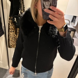 INTRESSEKOLL Svart jacka med fuskpäls - Snygg svart jacka med dragkedja och fuskpälsdetaljer på kragen. Perfekt för kyligare dagar. Jackan har en normal passform och långa ärmar.
