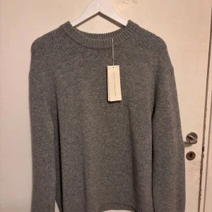 Grå stickad tröja från Arket - Säljer en stilren grå stickad tröja från Arket, tillverkad av 65% certifierad ansvarsfull ull. Aldrig använt pågrund av att jag inte gillar den oversized looken skulle säga att den är en klassisk M och man vill att den ska ha en mer normal passform 