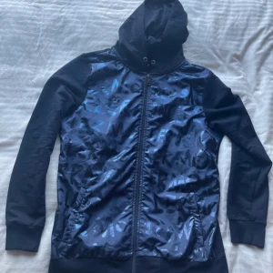 Mörkblå moncler jacka - Säljer en mörkblå jacka från moncler med glansigt mönster och dragkedja. Den har en huva med dragskedja och långa ärmar. Perfekt för en stilren look.