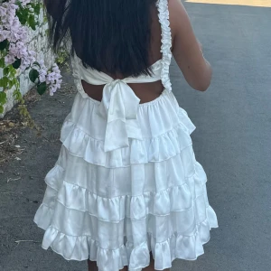Vit klänning med volanger - Charmig vit klänning med volanger och knytning i ryggen. Den har en smockad överdel och axelband med volangdetaljer. Perfekt för sommarens varma dagar eller studenten💗🤩