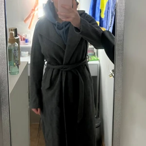 Grå kappa från BikBok - Snygg grå kappa från BikBok i storlek S. Den har en klassisk design med knytskärp i midjan och långa ärmar. Perfekt för kyligare dagar och ger en stilren look. Jag har knappt använd den då den är för stor för mig!🤍