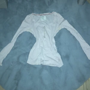 Ljusrosa långärmad topp med knappar - Säljer en ljusrosa långärmad topp med knappar framtill. Perfekt för en avslappnad stil och passar bra till jeans. Toppen har en rund halsringning och är i ett mjukt material.