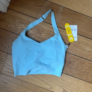 Ljusblå oneshoulder topp från Glowmode - Säljer en ljusblå halterneck topp från Glowmode. Toppen har en stilren design med justerbar rem och är perfekt för träning. Materialet är mjukt och stretchigt för bästa komfort. Iläggen går att ta bort🩵🩵🩵