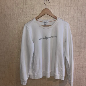 Vit tröja från Sail Racing - Vit tröja från Sail Racing med rund halsringning och tryckt logotyp på bröstet. Tröjan har långa ärmar och är tillverkad i ett mjukt material som ger en bekväm passform.