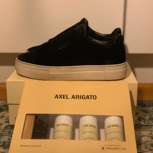 Svarta sneakers från Axel Arigato - Snygga svarta sneakers från Axel Arigato i mocka med en stilren design. Skorna har en vit sula och kommer med ett sneaker care kit för bästa vård. Perfekta för en trendig look. Skoprodukter+ 50 kr 