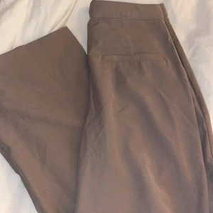 Beige kostymbyxor från 157 - Snygga beige kostymbyxor från 157 i storlek XS. Byxorna har en klassisk design med raka ben och en diskret ficka bak. Perfekta för en stilren look.