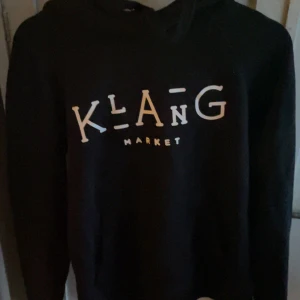 Svart hoodie från Klang Market - Säljer en svart hoodie från Klang Market med tryck på framsidan. Perfekt för en avslappnad stil. Den har en klassisk passform och är tillverkad i ett mjukt material.