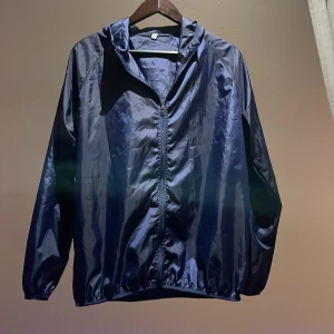 Svart vindjacka med huva - Säljer en stilren mörkblå vindjacka med dragkedja och huva. Jackan har en enkel design och är perfekt för blåsiga sommar dagar. Den är lätt och smidig att bära med sig det står att den är storlek XL men kommer passa någon med storlek S kommer inte passa någon med XL 👏🤩👏