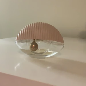 Kenzo world Parfym  med rosa lock och gulddetalj EDT - Kenzo World är elegant parfymflaska med ett unikt halvmåneformat design. Flaskan har ett ribbat rosa lock och en dekorativ guldfärgad kula. Den genomskinliga glasflaskan ger en lyxig känsla och gör det enkelt att se mängden parfym kvar.