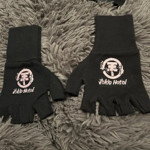 Svarta fingerlösa handskar med tryck - Snygga svarta fingerlösa handskar med ett coolt tryck i rosa och vitt. Perfekta för att ge en edgy look till din outfit. De är bekväma och lätta att bära, vilket gör dem till ett utmärkt val för både stil och funktion.