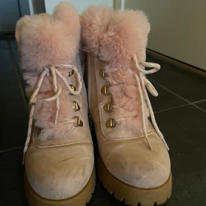 Pink boots med rosa pälsdetaljer - Säljer ett par snygga beige boots med rosa pälsdetaljer och snörning. De har en robust sula och guldiga snörhål som ger en extra touch. Perfekta för kyligare dagar.