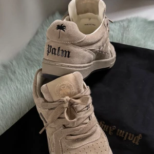 Beige sneakers från Palm Angels - Snygga beige sneakers från Palm Angels i mocka med broderad text och palm & angels på hälen. Skorna har snörning och perforerade detaljer på tån för extra stil. Perfekta för en avslappnad look. Köpta på NK, 